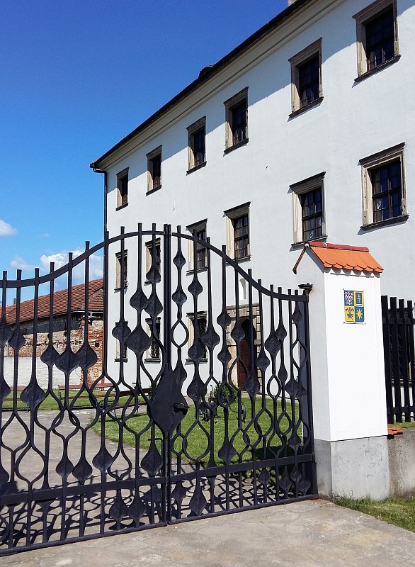 Pohled skrz kovanou bránou na muzeum v Rymicích